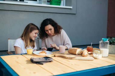 Anne ve kızı bahçede kahvaltıda teknoloji kullanıyorlar..