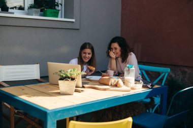 Anne ve kızı dışarıda oturmuş laptopta komedi filmi izlerken yemek yiyorlar..