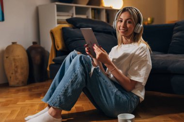 Güzel genç bayan yerde oturuyor ve tablet kullanıyor..