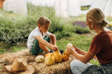 Çocuk samanlıkta otururken annesi aldığı farklı balkabaklarını gösteriyor..