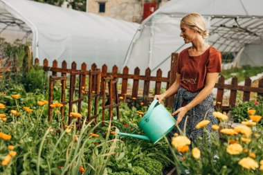 Bahçede çiçekleri sulayan mutlu beyaz kadın..