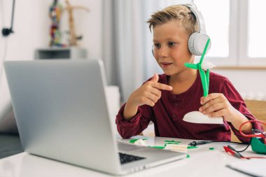 Bir ilkokul öğrencisi online sınıfta yel değirmeni modeli gösteriyor..