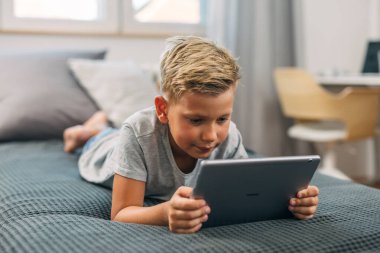 Tatlı bir çocuk yatakta tablet kullanmaktan hoşlanıyor..