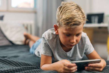 Bond Kafkasyalı çocuk yatakta cep telefonu kullanıyor..