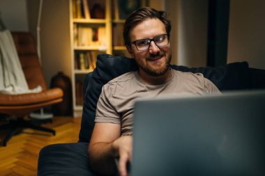 Akşamları evde dizüstü bilgisayar kullanan mutlu bir beyaz adam..