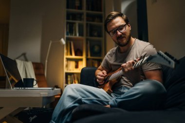 Beyaz adam evde tek başına gitar çalışıyor..