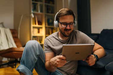 Neşeli adam evde yerde oturuyor ve tabletten bir şeyler izliyor..