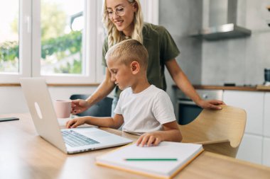 Çocuk internetten ders alıyor ve annesi ona sıcak içecek getiriyor..