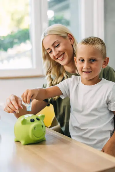 Happy mother and son saving money in a piggy bank.