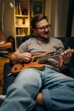 Koltukta oturup elektro gitar çalan bir adamın ön görüntüsü..