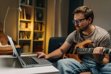 Beyaz adam internetten elektro gitar notlarını okuyor.