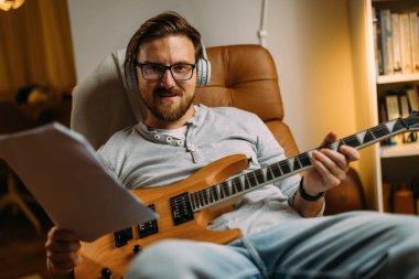 Elinde gitar ve notalar tutan müzisyenin ön görüntüsü.