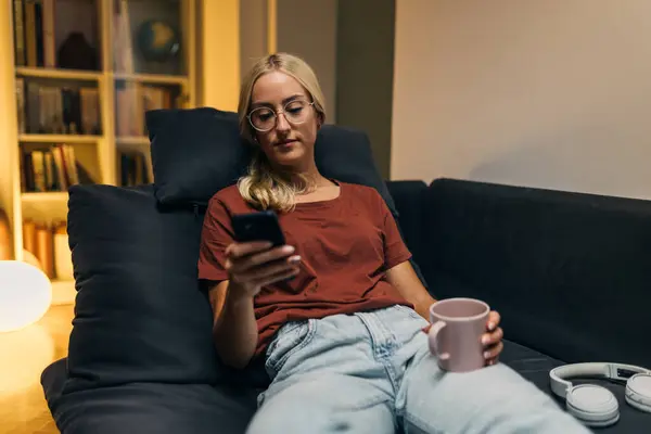 Front view of a relaxed woman sitting on the couch and using mobile phone in her living room.
