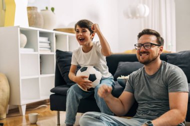 Genç çocuk ve babası evlerinden gelen futbol takımı için tezahürat yapıyorlar..
