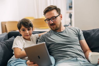 Kafkasyalı bir baba ve oğulun evdeki tablet ekrana baktığı ön manzara..