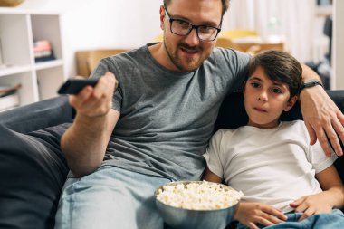 Baba ve oğulun birlikte televizyon izlemesi ön planda..