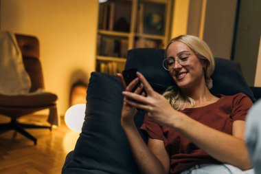 Kanepeye uzanmış telefonuna mesaj yazan bir kadın..