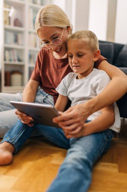 Genç beyaz bir çocuk annesinin yardımıyla tablet üzerinde oyun oynuyor..