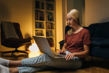 Sarışın kadın dizüstü bilgisayar kullanıyor ve akşamları evde dinleniyor..