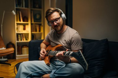 Yetişkin beyaz bir adam evde gitar çalıyor..