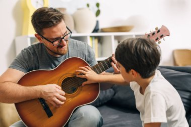 Oğlu tellerle çalarken babası gitarı tutuyor..