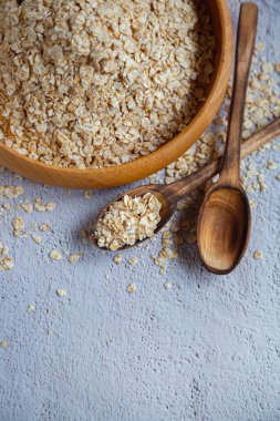 Hafif arka planda yulaf ezmeli ahşap kaşık ve bir tabak dolusu yulaf ezmesi.