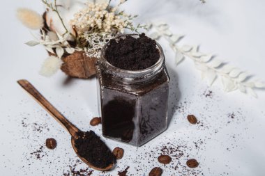 Glass jar with coffee scrub, wooden spoon on a light background. Homemade ingredients for body scrubs