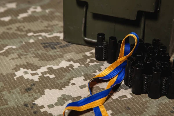 Military green box, machine gun ribbon and blue-yellow ribbon, colors of the Ukrainian flag, on the background of the green military pixel.