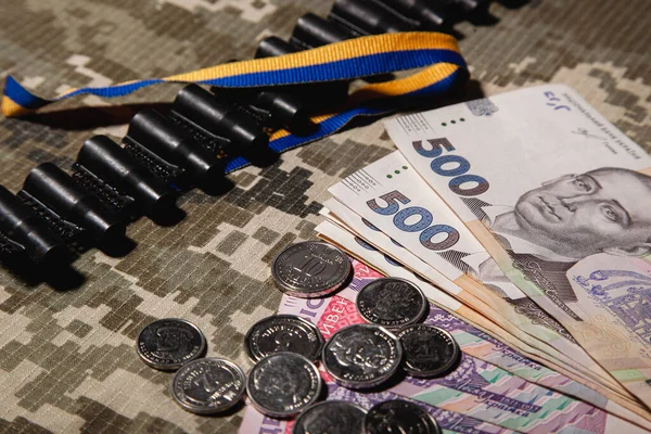 500 Hryvnia banknotları ve 10 Hryvnia değerinde bozuk paralar ve diğerleri, askeri pikselin arka planında makineli tüfek bandı ve mavi-sarı. Ukrayna Hryvnia 'sı. Ukrayna 'nın parası.