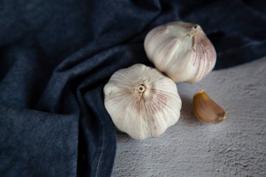 Gri arka planda iki büyük baş sarımsak ve mavi bir mutfak havlusu.