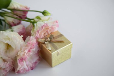 Hediyeli bir altın kutu, beyaz arka plandaki çiçeklerin yanında bir sürpriz.