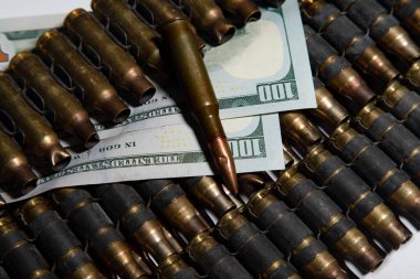 Amerikan dolarlarının üzerinde duran mermi ve mühimmat kovanlarını gösteren bir fotoğraf.