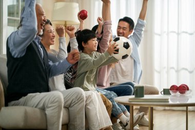 Üç kuşak Asyalı aile evlerinde kanepede oturmuş maç canlı yayınlarını izlerken gol ve zaferi kutluyorlar.