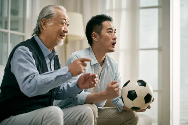 亚洲的年长父亲和成年儿子一起在电视上看足球比赛 — 图库照片