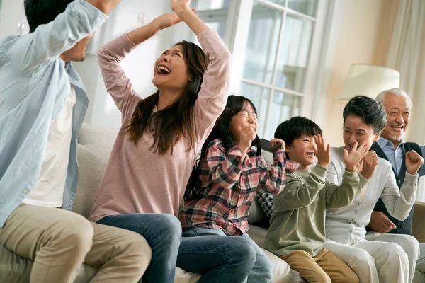 Trzy Pokolenia Azjatyckiej Rodziny Siedzi Kanapie Domu Świętując Cel Zwycięstwo — Zdjęcie stockowe