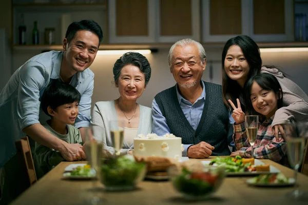 three generation asian family gathering at home celebrating senior couple\'s wedding anniversary