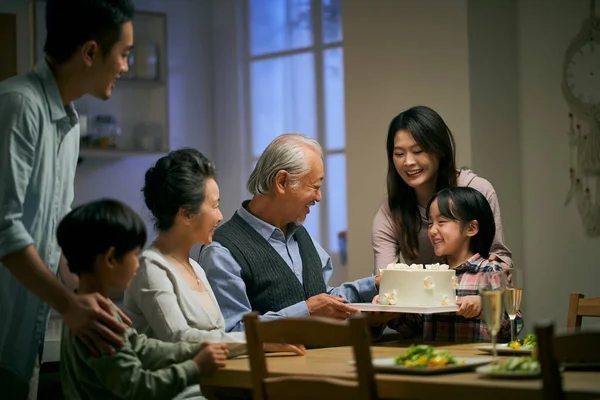 three generation asian family gathering at home celebrating senior couple's wedding anniversary