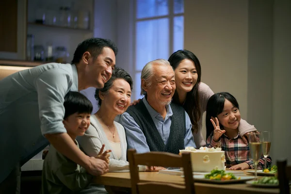 three generation asian family gathering at home celebrating senior couple\'s wedding anniversary