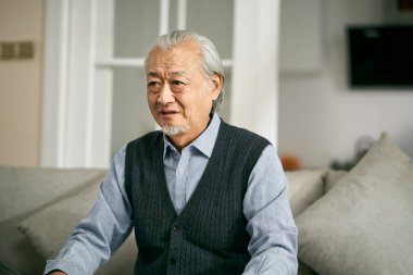 Asyalı üzgün adam oturma odasında kanepede oturup ağlıyor.