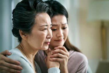 grieving senior asian mother and adult daughter holding hands