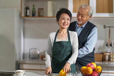 loving senior asian man husband helping wife tying up apron in kitchen at home
