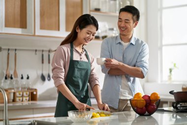 loving young asian couple chatting talking conversing in kitchen at home while preparing food