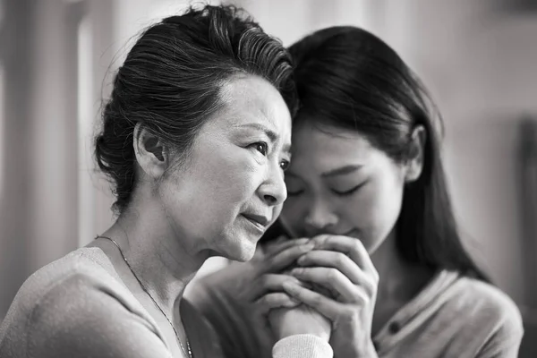 young asian adult daughter consoling senior mother living with mental illness, black and white