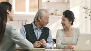 senior asian couple appears to be convinced and happy signing a paper document at home