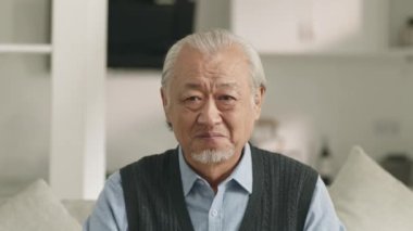 sad senior asian man sitting on couch at home weeping