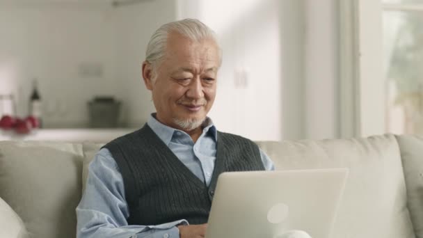 Старший Азіатський Чоловік Сидить Дивані Вдома Використовуючи Ноутбук — стокове відео