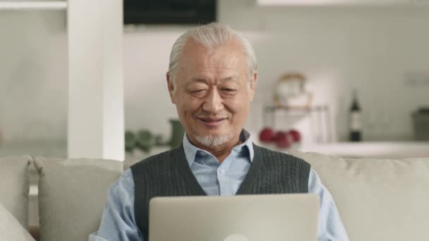 Starszy Azji Człowiek Siedzi Kanapie Domu Pomocą Laptopa — Wideo stockowe