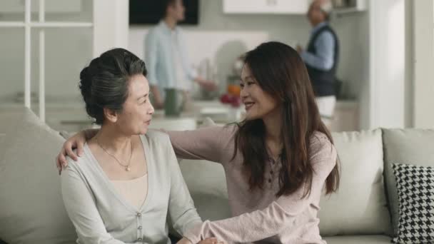 二人の夫が背景で話している間若いアジアの女性は訪問中にお母さんとおしゃべりをしました — ストック動画