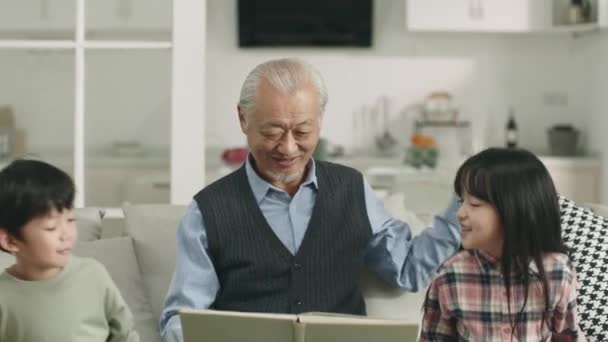 アジアのおじいちゃんは孫2人と一緒に本を読んで — ストック動画
