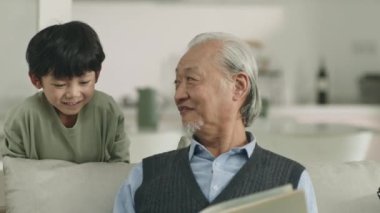 asian grandpa and grandson chatting talking reading book together